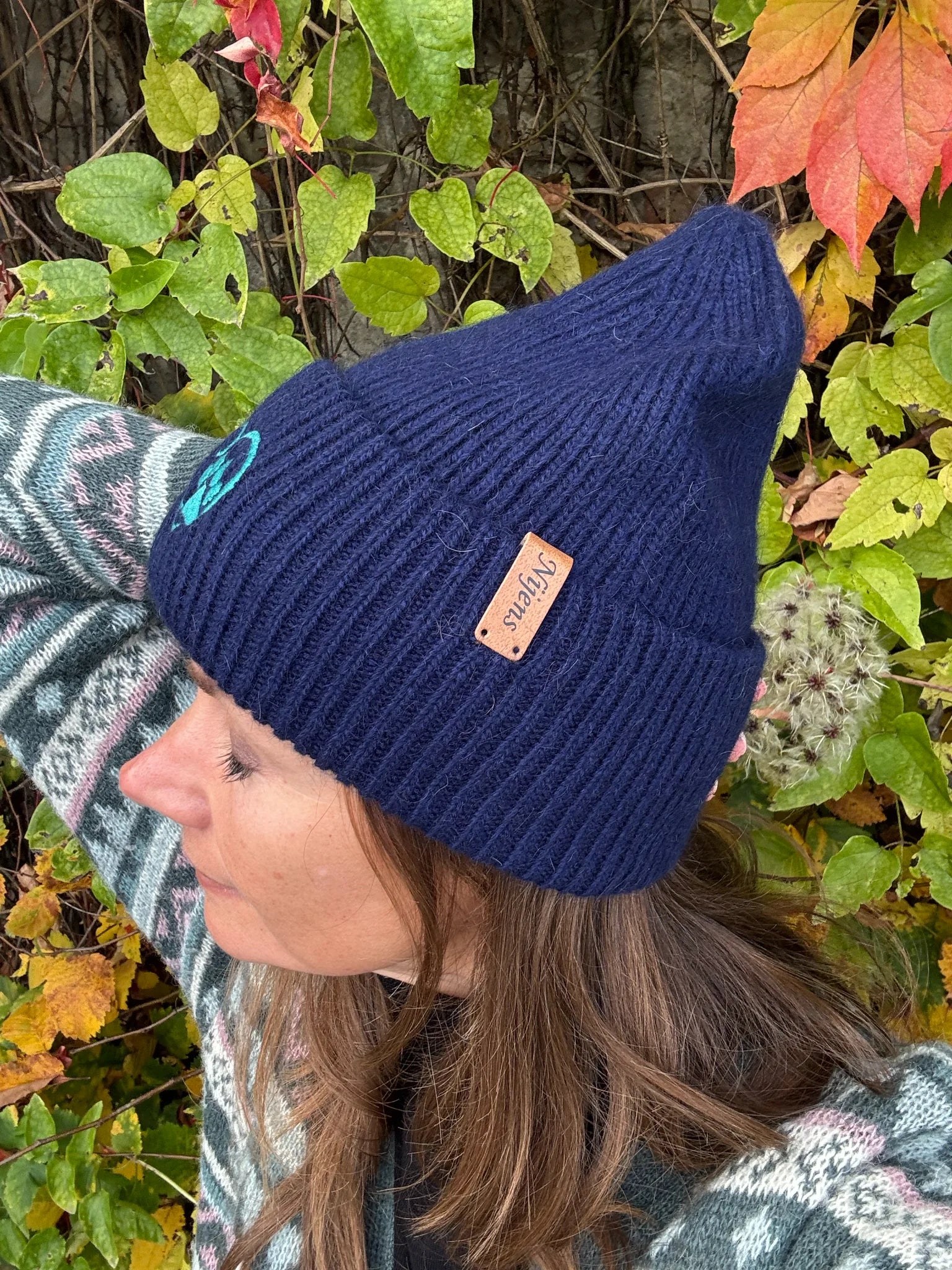 Seitliche Ansicht einer Frau mit dunkelblauer Nijens Angora Beanie Marseille und Pfote-&-Herz-Stickerei vor herbstlichem Hintergrund