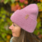 Seitliche Ansicht einer Frau mit Nijens Angora Beanie in Rosa und Pfote-&-Herz-Stickerei vor herbstlichem Hintergrund