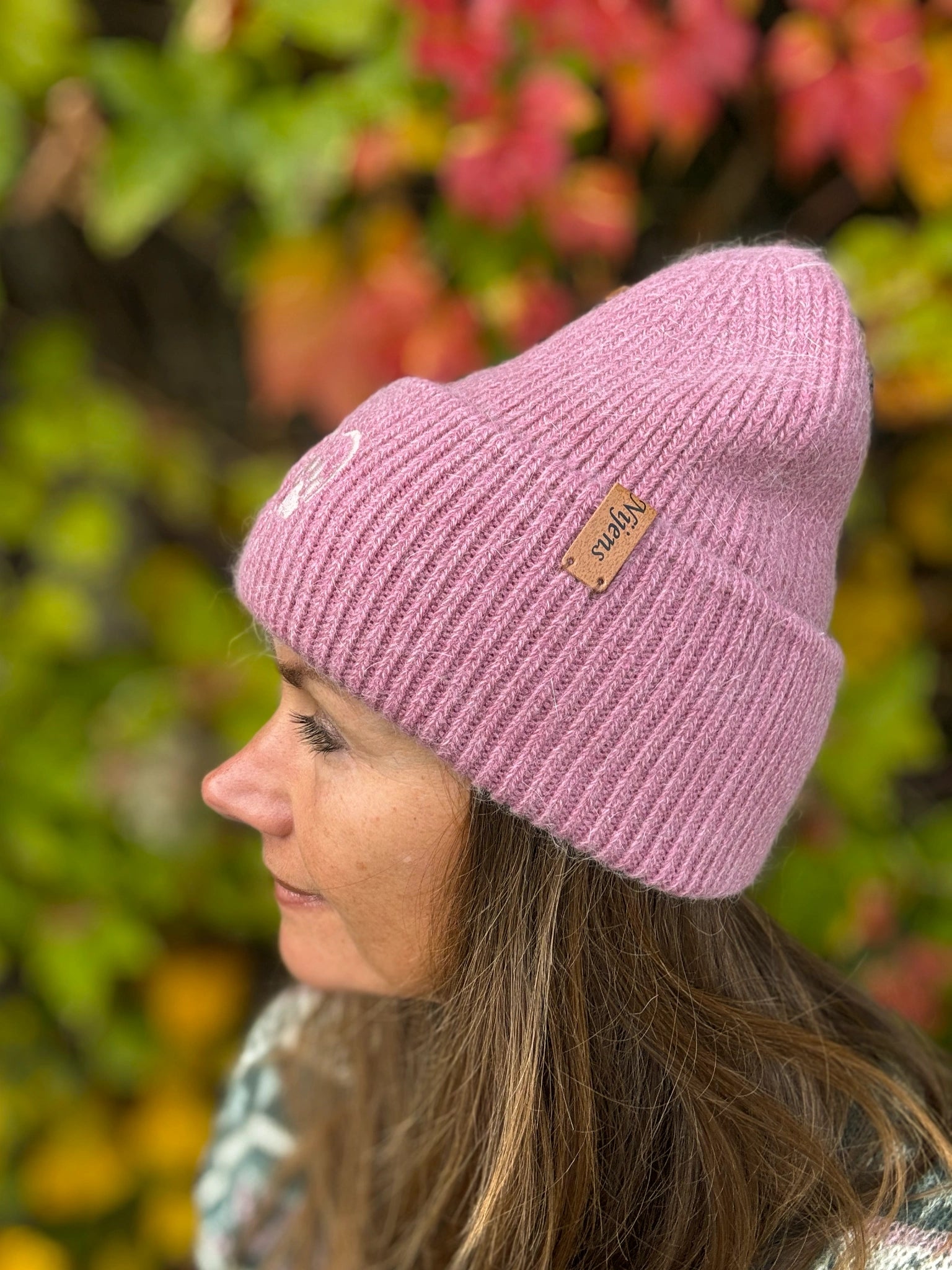 Seitliche Ansicht einer Frau mit Nijens Angora Beanie in Rosa und Pfote-&-Herz-Stickerei vor herbstlichem Hintergrund