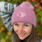 Frontansicht einer Frau mit Nijens Angora Beanie in Rosa und Pfote-&-Herz-Stickerei vor herbstlichem Hintergrund