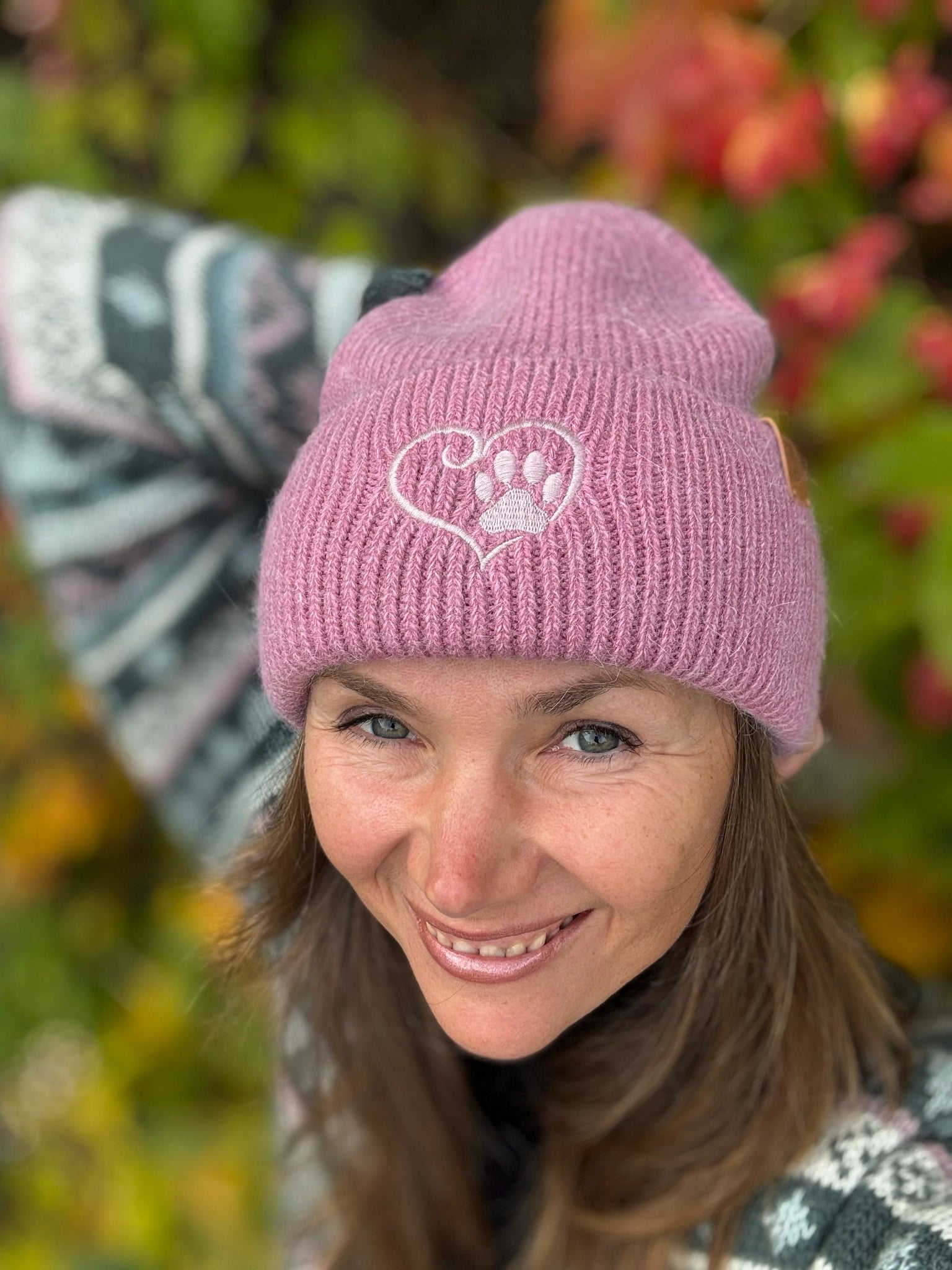 Frontansicht einer Frau mit Nijens Angora Beanie in Rosa und Pfote-&-Herz-Stickerei vor herbstlichem Hintergrund