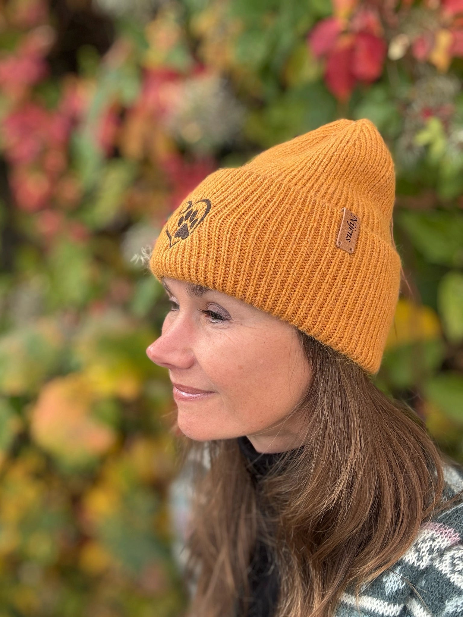 Frau trägt orange Nijens Angora Beanie Marseille mit Pfote-&-Herz-Stickerei beim herbstlichen Spaziergang