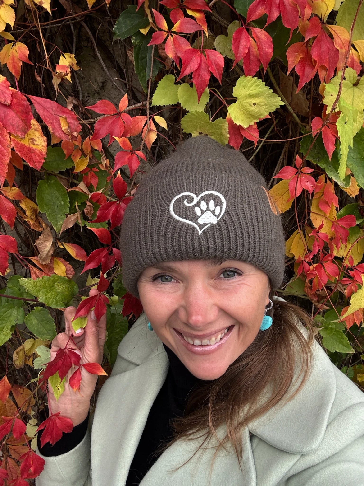 Frau trägt olivgrüne Nijens Angora Beanie Marseille mit Pfote-&-Herz-Stickerei beim herbstlichen Spaziergang