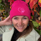 Eine Frau trägt Nijens Beanie Leonberg aus Acryl Fuchsia mit umgeschlagenem Rand mit Pfote und Herz Stickerei