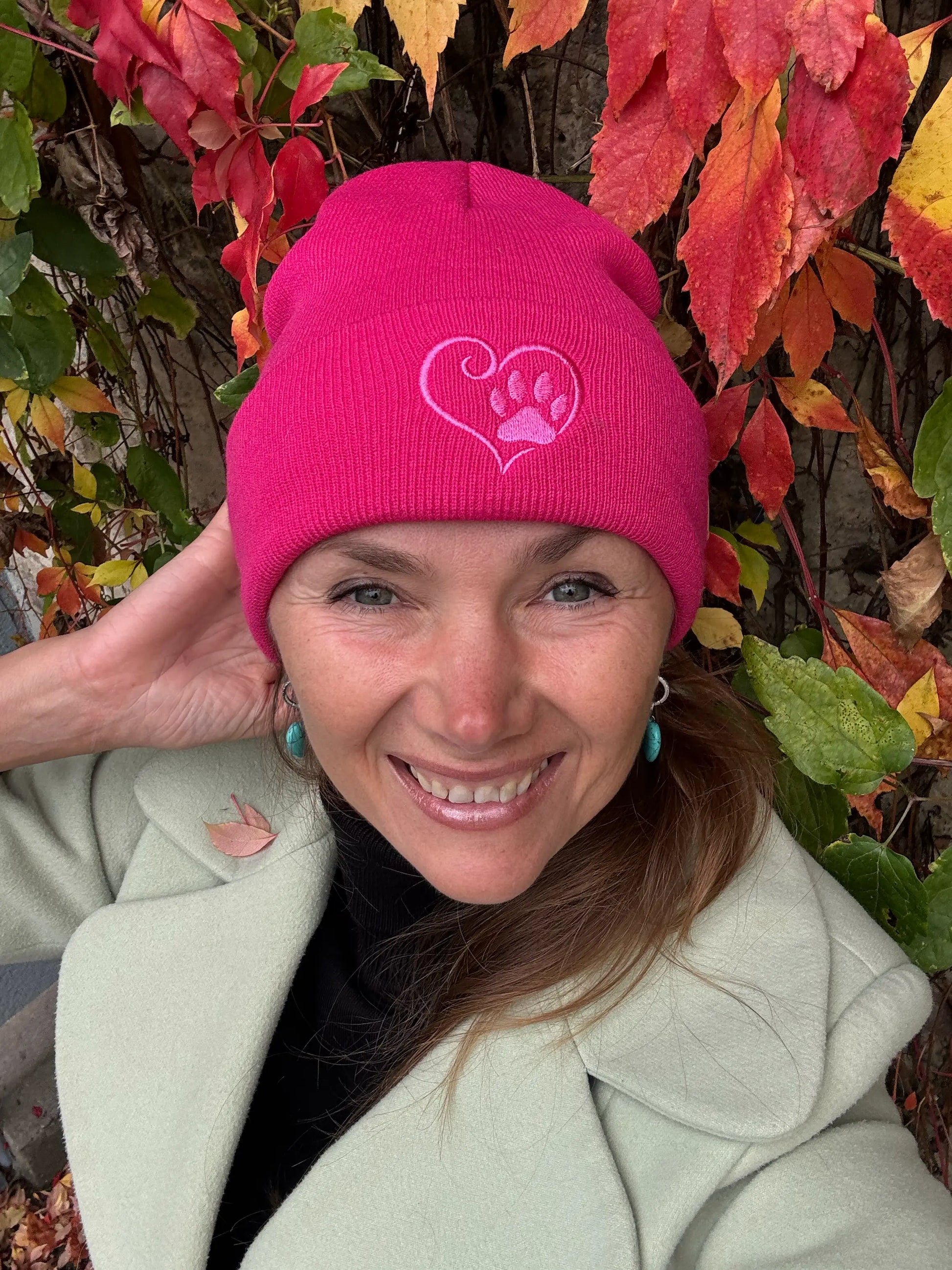 Eine Frau trägt Nijens Beanie Leonberg aus Acryl Fuchsia mit umgeschlagenem Rand mit Pfote und Herz Stickerei