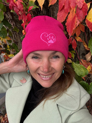 Eine Frau trägt Nijens Beanie Leonberg aus Acryl Fuchsia mit umgeschlagenem Rand mit Pfote und Herz Stickerei
