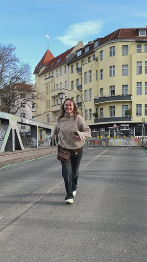 Frau trägt schokobraune Gassitasche aus Canvas mit echtem Leder als Crossbody in der Berliner Innenstadt und zeigt die Reißverschlussfächer unterwegs.