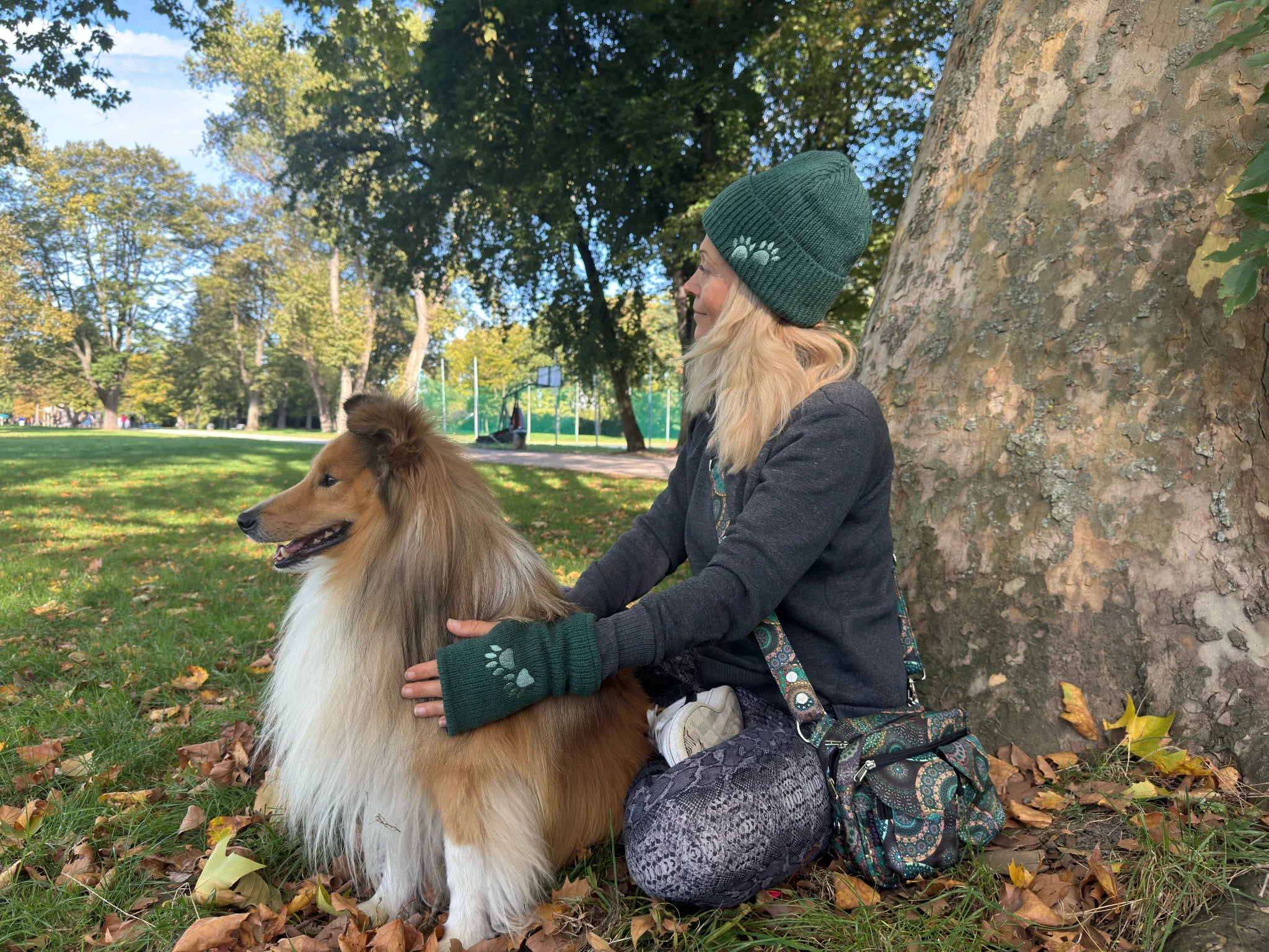 Hundebesitzerin mit Hund auf einer Wiese und Outfit von Nijens: Handstulpen und Mütze mit Pfotenaufdruck sowie einer Gassitasche